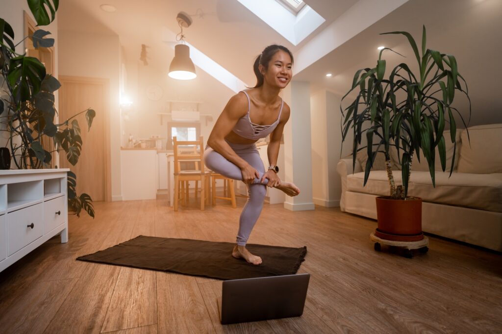 Beautiful Asian woman training fitness at home and using laptop