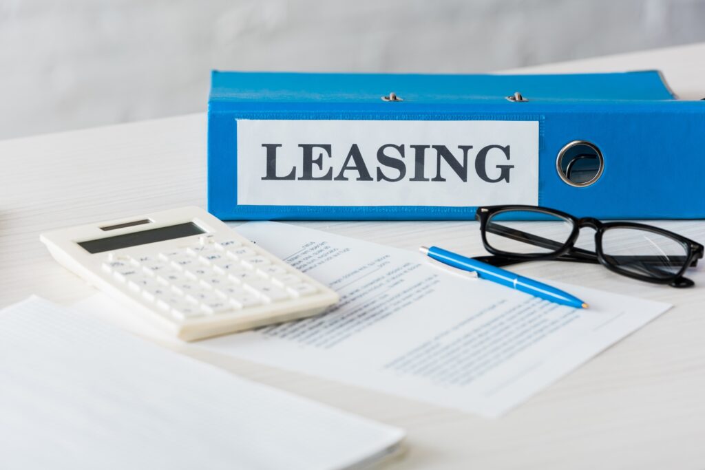 selective focus of folder with leasing lettering near calculator, pen and glasses on desk