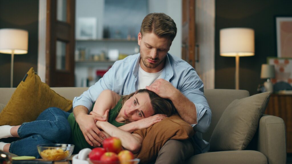 Gentle man regretting woman crying at sofa. Calm guy comforting beloved lady